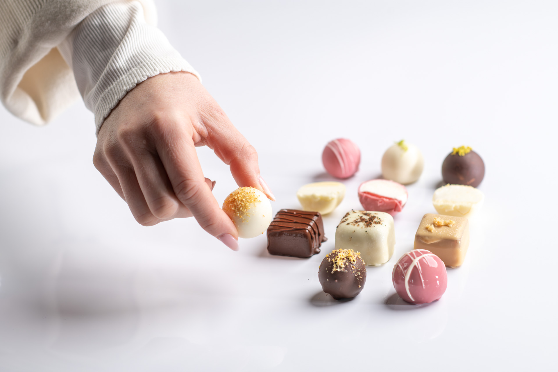 Hand greift eine feine Praline aus einer Auswahl handgefertigter Pralinen