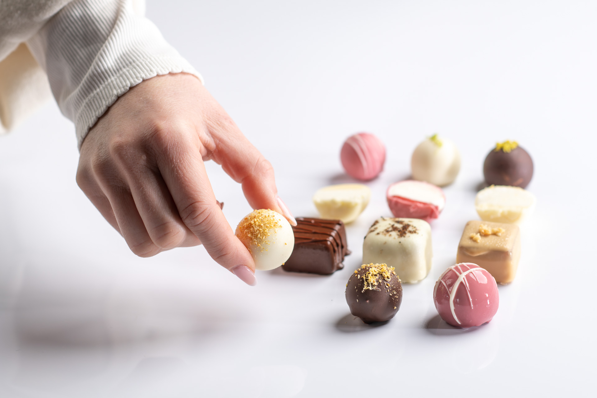 Hand, die eine feine Praline aus einer Auswahl handgefertigter Pralinen nimmt