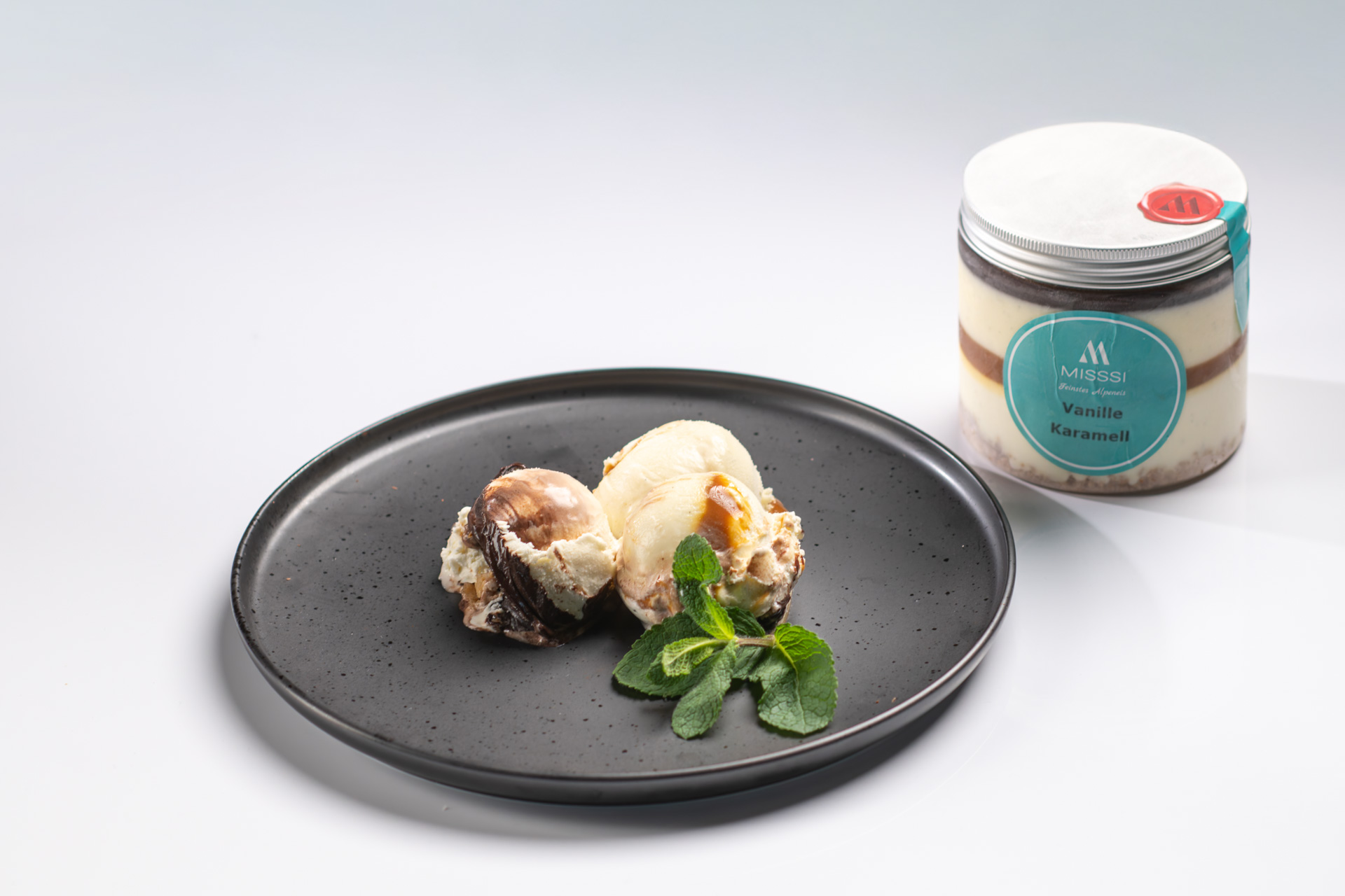 Zwei Eiscreme-Kugeln mit Schokolade und Karamell auf einem dunklen Teller, garniert mit frischer Minze